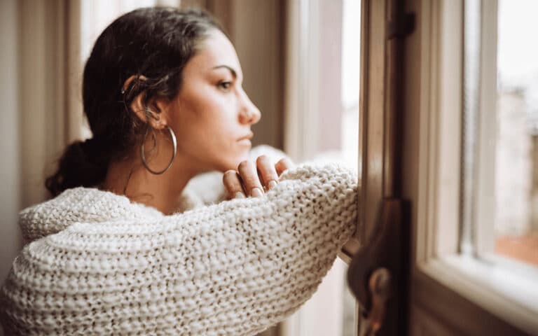 woman in sweater looking out the window of a home