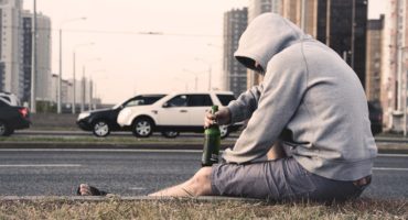 man drinking beer on curb